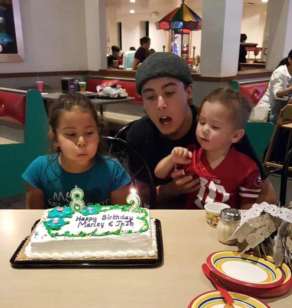 A man and two children blowing out candles on a cake.