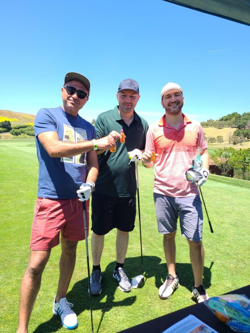 Three men are standing on a golf course holding their clubs.