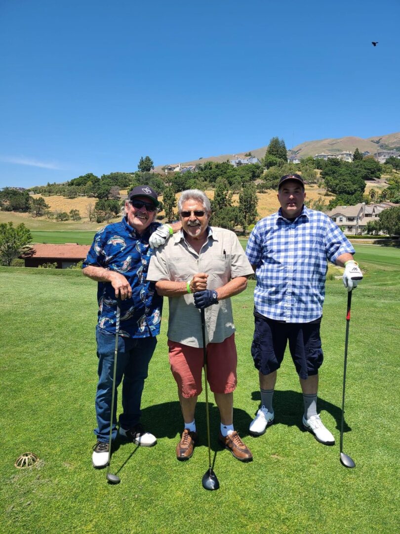 Three men standing on a golf course holding onto their clubs.