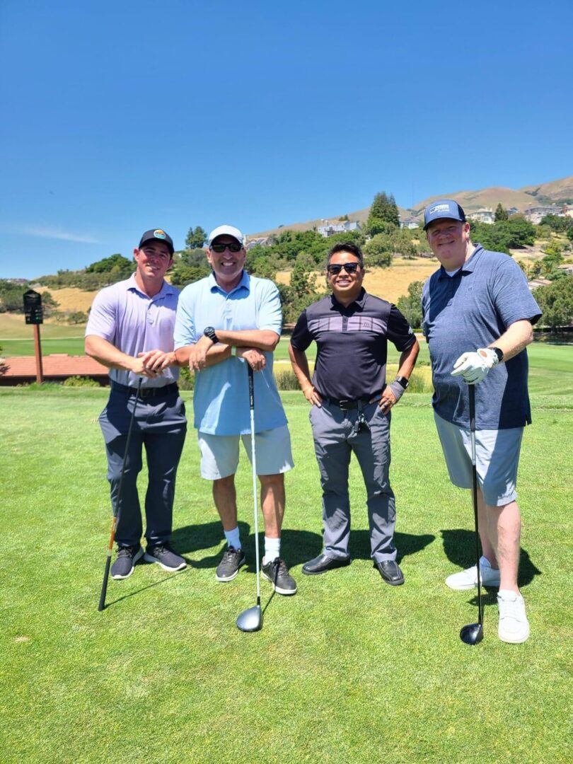 Four men standing on a golf course holding onto their clubs.