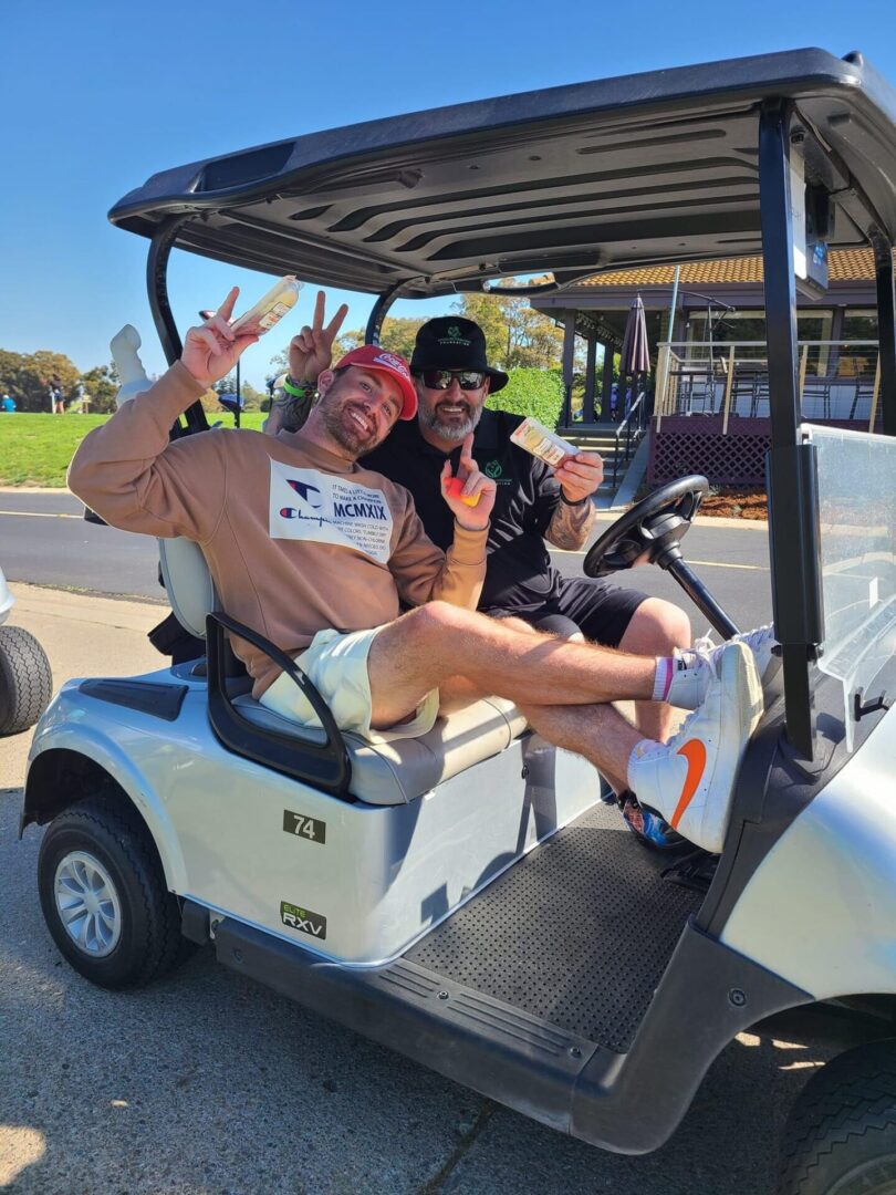 Two men in a golf cart with one holding up the peace sign.