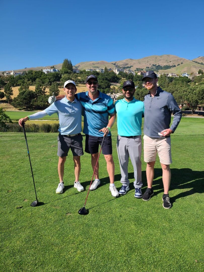 Four men standing on a golf course with their golf clubs.